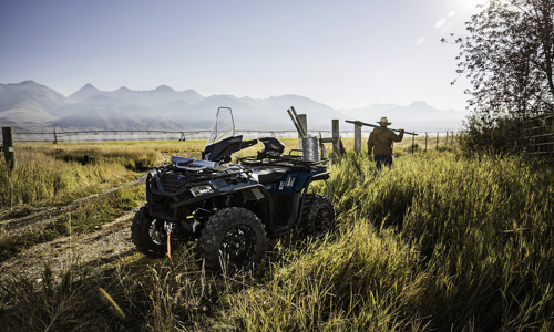 A person repairs a barbed wire fence with a Polaris Sportsman® ATV parked nearby