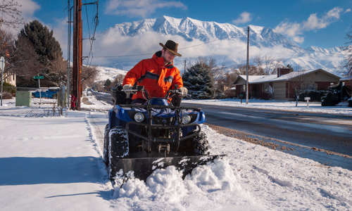 A man is removing the snow in an ATV with a snowplow.