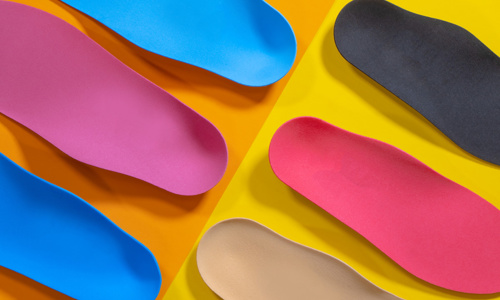 Different colors of orthopedic insoles for shoes on colorful background.