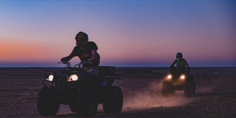 two people riding ATV's at sunset
