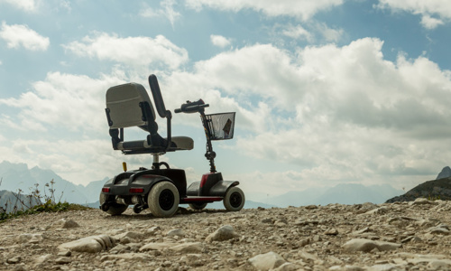 A mobility scooter on a mountain, white clouds and blue sky in the background.