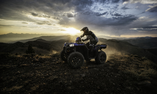 A man is riding in a Polaris® ATV in the mountains a sunset.