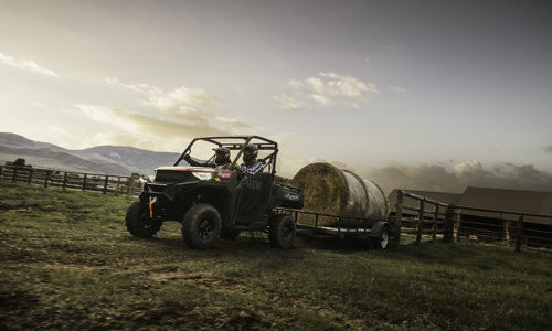 Two men are riding in a Polaris® UTV towing a trailer whit hay.